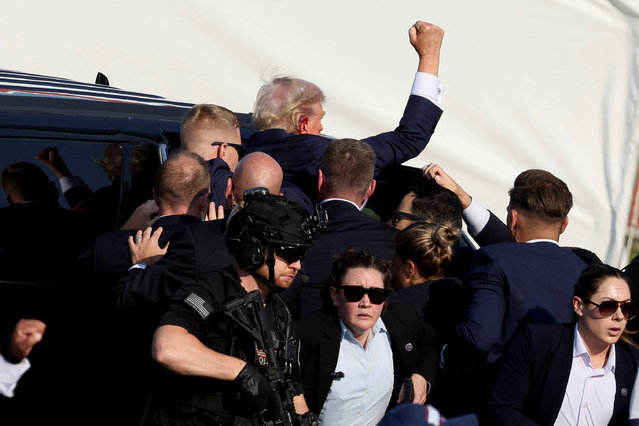 Trump gestures as he gets into a vehicle with the assistance of Secret Service personnel on July 13, 2024. (Photo by Brendan McDermid/Reuters)