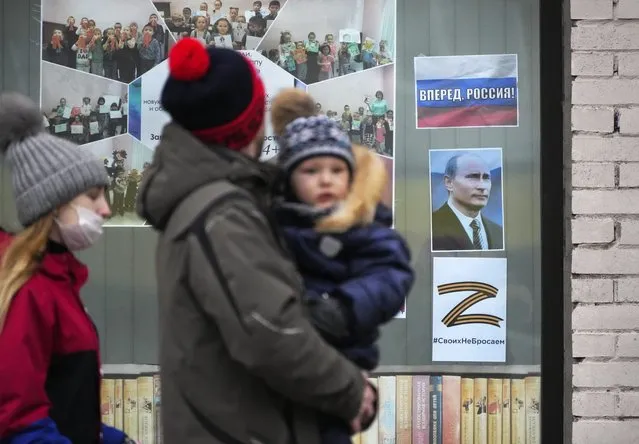 A family walk past a portrait of Russian President Vladimir Putin, a sign reading “Go Russia!” and the letter Z, which has become a symbol of the Russian military, displayed in the window of a children's library in St. Petersburg, Russia, Friday, March 11, 2022. (Photo by AP Photo, File)