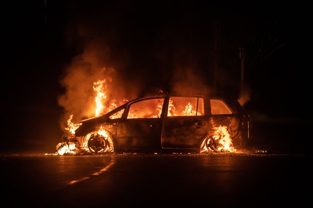 This photograph shows a car on fire on Riviere Salee's main road in Noumea, in the French Pacific territory of New Caledonia, on June 24, 2024. A fresh surge of unrest hit the French Pacific territory of New Caledonia, with several buildings set on fire overnight, including a police station and a town hall, authorities said on June 24, 2025. In mid-May, rioting and looting erupted in New Caledonia over an electoral reform plan that Indigenous Kanak people feared would leave them in a permanent minority, putting independence hopes definitively out of reach. (Photo by Delphine Mayeur/AFP Photo)