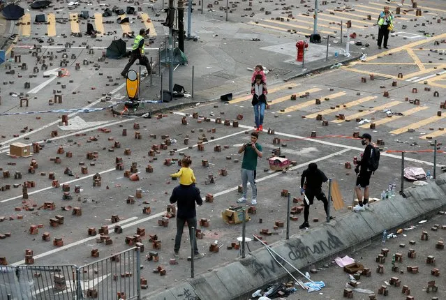 A man poses for a picture with a child on his shoulders among bricks scattered on the street outside the Polytechnic University in Hong Kong, November 15, 2019. The Cross-Harbour Tunnel, outside the barricaded Polytechnic University where protesters have practiced firing bows and arrows and throwing petrol bombs in a half-empty swimming pool, remained shut. (Photo by Adnan Abidi/Reuters)