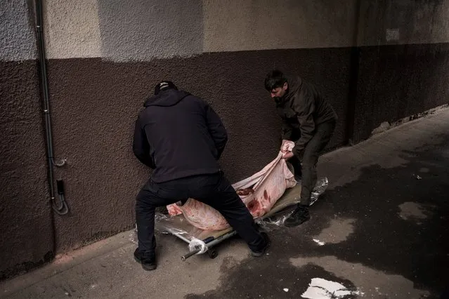 People remove the body of an elderly woman killed in a Russian bombardment in downtown Kharkiv, Ukraine, Sunday, April 17, 2022. (Photo by Felipe Dana/AP Photo)