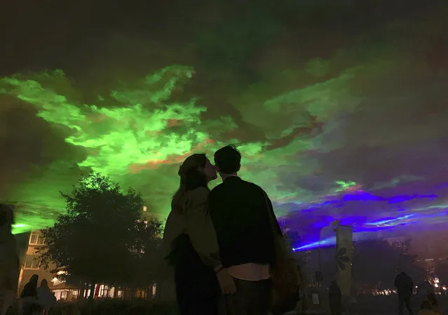 Two people embrace in a public square as they watch an art installation by artist Dan Acher called Borealis in the center of Antwerp, Belgium, Sunday, August 29, 2021. (Photo by Virginia Mayo/AP Photo)