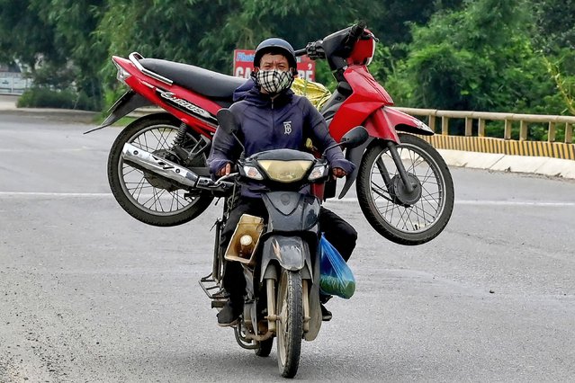 A man rides a motorbike while transporting a motorbike along a road in Hanoi on May 28, 2024. (Photo by Nhac Nguyen/AFP Photo)