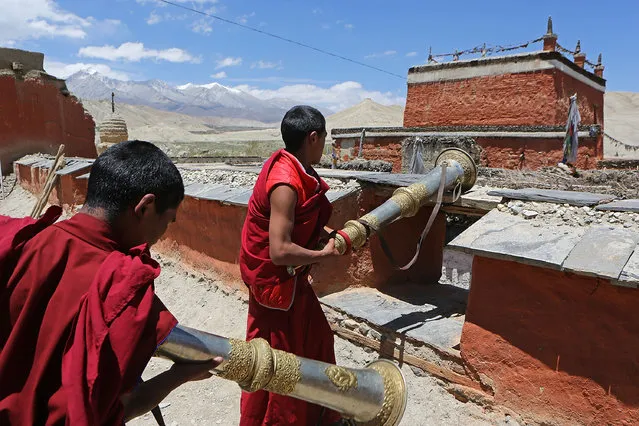 Monks set up dungchen, Tibetan ritual horns, on a monastery rooftop at the end of a ceremony during the Tenchi Festival on May 25, 2014 in Lo Manthang, Nepal. The Tenchi Festival takes place annually in Lo Manthang, the capital of Upper Mustang and the former Tibetan Kingdom of Lo. Each spring, monks perform ceremonies, rites, and dances during the Tenchi Festival to dispel evils and demons from the former kingdom. (Photo by Taylor Weidman/Getty Images)