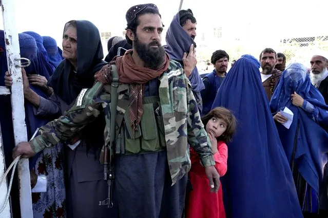 A Taliban fighter stands guard as people receive food rations distributed by a Saudi humanitarian aid group, in Kabul, Afghanistan, Monday, April 25, 2022. (Photo by Ebrahim Noroozi/AP Photo)