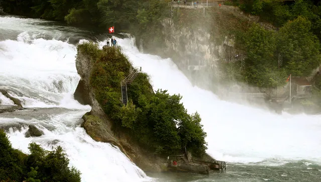 Tourists stand under a Swiss national flag atop an island in between the Rhine Falls, the largest falls in Europe, in the town of Neuhausen, Switzerland July 25, 2017. (Photo by Arnd Wiegmann/Reuters)