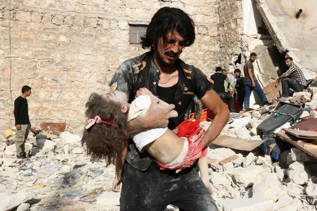 A Syrian man carries a child who was retrieved under the rubble of a collapsed building following a reported air strike on the rebel-held neighbourhood of Sakhur in the northern city of Aleppo on July 19, 2016. Civilians in rebel-held parts of Syria's Aleppo expressed fears on July 18, 2016 of a lengthy government siege, as food supplies dwindled after regime troops seized the only road into the city's east. The government advance, which has been backed by a Russian air offensive, is seen as a major setback for opposition forces in Syria's second city. (Photo by Thaer Mohammed/AFP Photo)