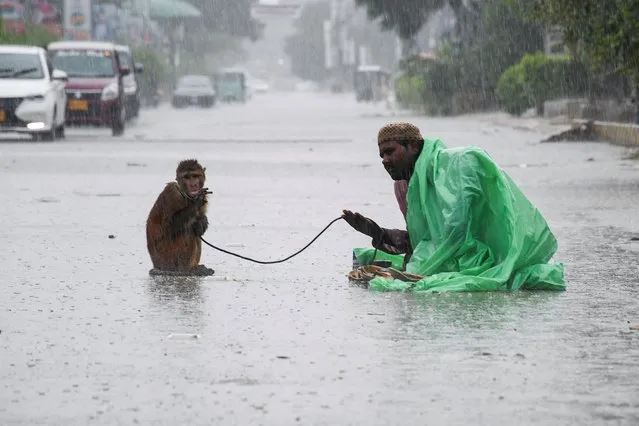 A man sits with his pet monkey, as they seek charity from passersby, along a road amidst rainfall during the monsoon season in Hyderabad, Pakistan on August 24, 2022. (Photo by Yasir Rajput/Reuters)