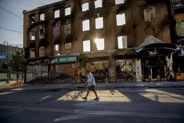 A man walks past a damaged building following overnight protests over the death of George Floyd, Sunday, May 31, 2020, in Minneapolis, Minn.  Protests were held throughout the country over the death of Floyd, a black man who died after being restrained by Minneapolis police officers on May 25.  (Photo by Elizabeth Flores/Star Tribune via AP Photo)