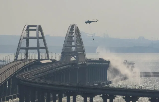 A helicopter drops water to extinguish fuel tanks ablaze on the Kerch bridge in the Kerch Strait, Crimea on October 8, 2022. (Photo by Reuters/Stringer)