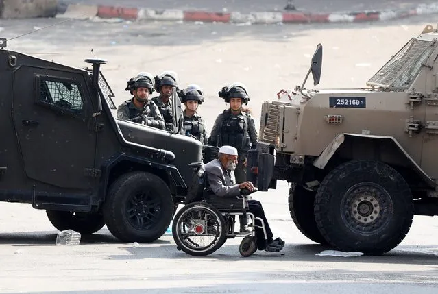 An elderly Palestinian man on wheelchair passes in front of Israeli soldiers at the site of clashes with protesters in the West Bank city of Hebron, 12 October 2022. Palestinians called for protests and a general strike across West Bank cities, including Hebron, in solidarity with Palestinians in Jerusalem's Shufat camp, where more than 100,000 people had been under tight Israeli army siege for four days due to the closure of the checkpoints. (Photo by Abed Al Hashlamoun/EPA/EFE)