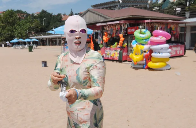 A woman wearing a facekini mask at the beach during a heatwave in the area Qingdao City, China on August 17, 2016. Many middle-aged women wear the masks to protect the skin from the sun and jellyfish and algae. (Photo by Sipa Asia/Rex Features/Shutterstock)