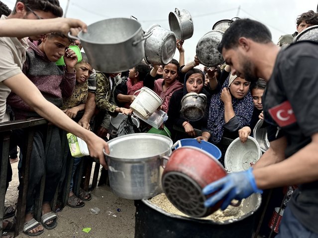 Palestinians, who have difficulty finding food, wait with empty pots and pans in their hands to receive meals distributed by charitable organizations at Al-Mawasi in Khan Yunis, Gaza on April 02, 2025. (Photo by Doaa Albaz/Anadolu via Getty Images)