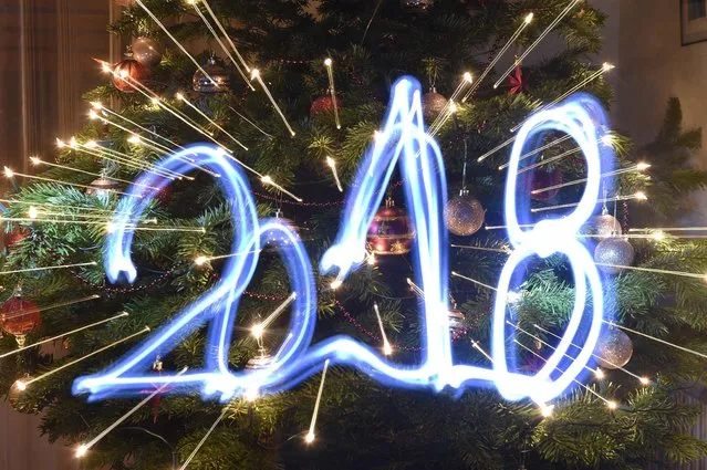 This illustration taken with a long time exposure and with zoom effect on December 31, 2017 in Budapest, Hungary, shows the year “2018”, painted with a flashlight in front of a Christmas tree. (Photo by Attila Kisbenedek/AFP Photo)