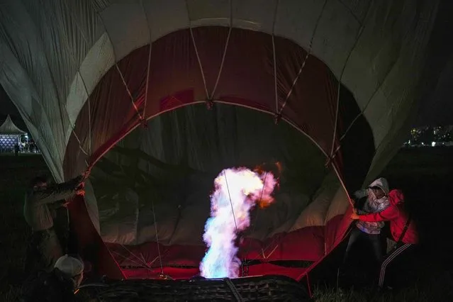 A crew inflates a hot air balloon during the Expo Transporte at La Carlota air base in Caracas, Venezuela, Friday, December 9, 2022. (Photo by Matias Delacroix/AP Photo)