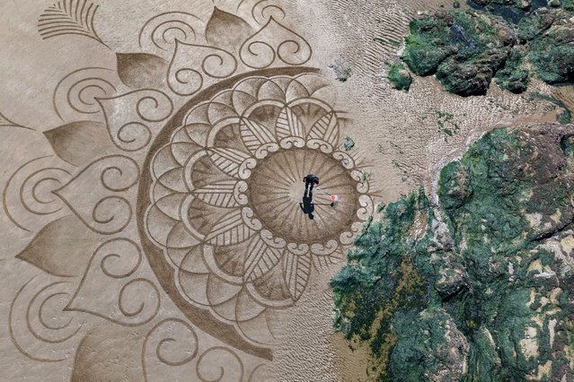 A drone view shows French artist Pierre-Louis Cullier drawing a mandala with a rake on the sand near seaweed-covered rocks, on a beach on the France's Atlantic coast in Saint-Michel-Chef-Chef, France, on June 17, 2025. (Photo by Stephane Mahe/Reuters)