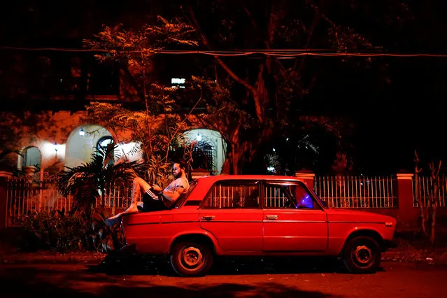 Tourist guide Daniel Hernandez, 26, sits on his Russian-made car as he speaks to his girlfriend who lives in Britain, at an internet hotspot in Havana, Cuba, September 24, 2017. (Photo by Alexandre Meneghini/Reuters)