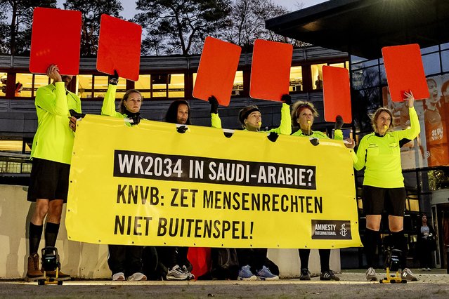 Amnesty International activists dressed as football referees hold red cards and a banner reading “World Cup in Saudi Arabia? KNVB: Do not sideline human rights” in front of the Royal Dutch Football Association KNVB headquarters during a protest against Saudi Arabia's candidacy for the 2034 World Cup, in Zeist on November 11, 2024. (Photo by Robin van Lonkhuijsen/ANP via AFP Photo)