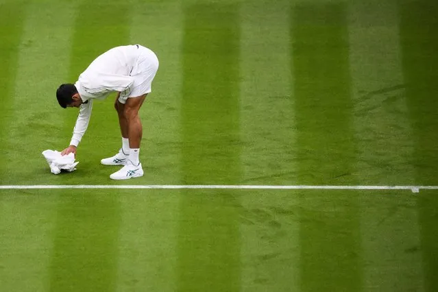 Serbia's Novak Djokovic jokes as he attempts to dry the grass of Center Court with a towel as the rains starts to fall during his men's singles tennis match against Argentina's Pedro Cachin on the first day of the 2023 Wimbledon Championships at The All England Tennis Club in Wimbledon, southwest London, on July 3, 2023. (Photo by Daniel Leal/AFP Photo)