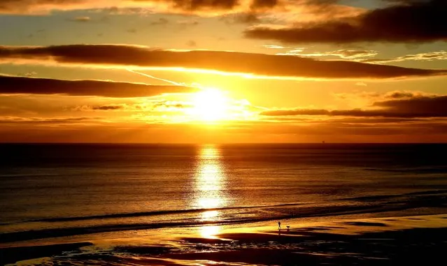 Dog walkers during sunrise on Longsands beach in Tynemouth on October 23, 2014. (Photo by Owen Humphreys/PA Wire)