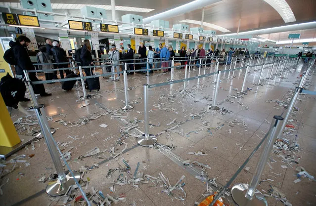 Passengers queue in front of Vueling check-in desks as the floor is littered with pieces of paper during a protest by the cleaning staff at Barcelona's airport, Spain, December 1, 2016. (Photo by Albert Gea/Reuters)