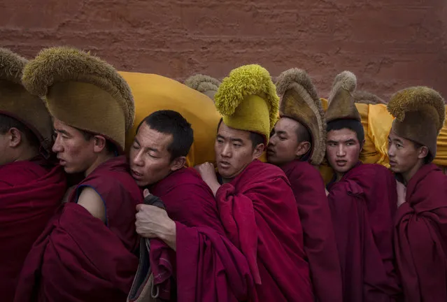 Tibetan Buddhist Monks of the Gelug, or Yellow Hat order, carry a large thangka of Buddha after showing it to worshippers during Monlam or the Great Prayer rituals on March 3, 2015 at the Labrang Monastery, Xiahe County, Amdo, Tibetan Autonomous Prefecture, Gansu Province, China. (Photo by Kevin Frayer/Getty Images)