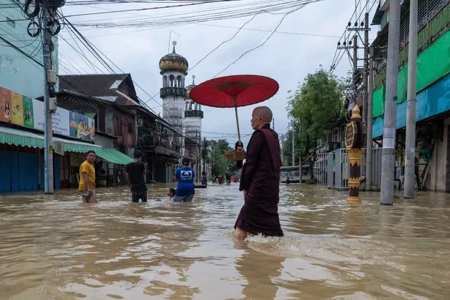A Buddhist monk wades through a flooded street following monsoon rains in Bago township, Bago region, on August 11, 2023. Floods and landslides caused by monsoon rains have killed five people and forced the evacuation of around 40,000 others in Myanmar, officials said on August 11. (Photo by Sai Aung Main/AFP Photo)