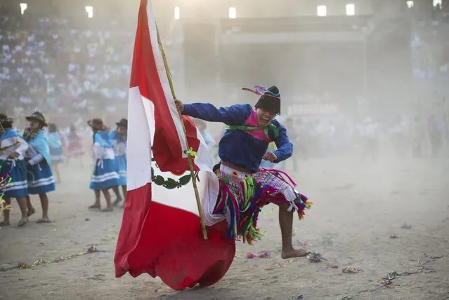 In this Sunday, March 29, 2015 photo, a man from the La Mar district of Ayacucho sings in Quechua, holding a Peruvian national flag as he performs in the Vencedores de Ayacucho dance festival, in the Acho bullring in Lima, Peru. The different dance troupes that perform during the one-day competition typically bring a representation of Peru's national flag to assert their nationality as well as their ethnic background. (Photo by Rodrigo Abd/AP Photo)