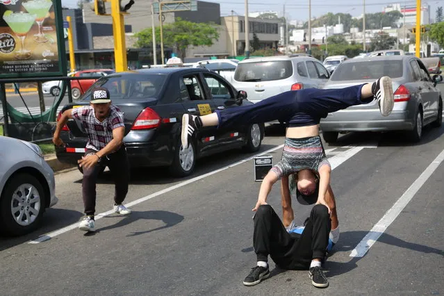 In this December 12, 2018 photo, Venezuelan breakdancers Maria Molina, right, Alex Beltran, on the ground, and Miguel Angel Flores perform for tips from commuters in Lima, Peru. With a captive audience of pedestrians and commuters, the dancers' headstands, spins and steps on a good day net up to $20 in pocket change, nearly three times the monthly minimum wage in Venezuela. (Photo by Cesar Olmos/AP Photo)