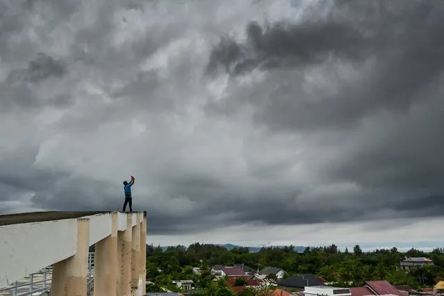 A man takes photos of dark clouds from a tsunami evacuation building on December 25, 2023, on the eve of the 19th anniversary of the 2004 Indian Ocean earthquake and tsunami, which killed over 200,000 people in 14 countries, with Aceh recording the highest death toll in Banda Aceh. (Photo by AFP Photo/Stringer)