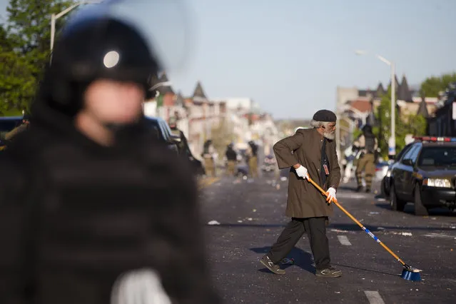 Residents clean streets as law enforcement officers stand guard, Tuesday, April 28, 2015, in Baltimore, in the aftermath of rioting following Monday's funeral of Freddie Gray, who died in police custody. (Photo by Matt Rourke/AP Photo)