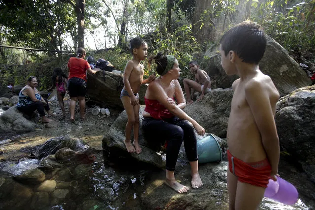 People bath at a brook in Caracas, Venezuela, Wednesday, March 27, 2019. After days of intermittent electricity supply in Venezuela, which affects the water supply, the people in the capital city have started to collect water from waterfalls and wells and carry it to their homes. (Photo by Boris Vergara/AP Photo)