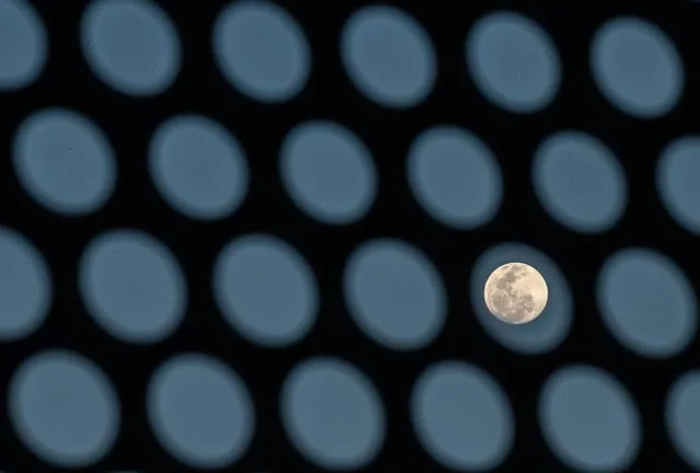 The full moon is seen behind a building's sun shade in Bangkok on January 9, 2020. (Photo by Mladen Antonov/AFP Photo)