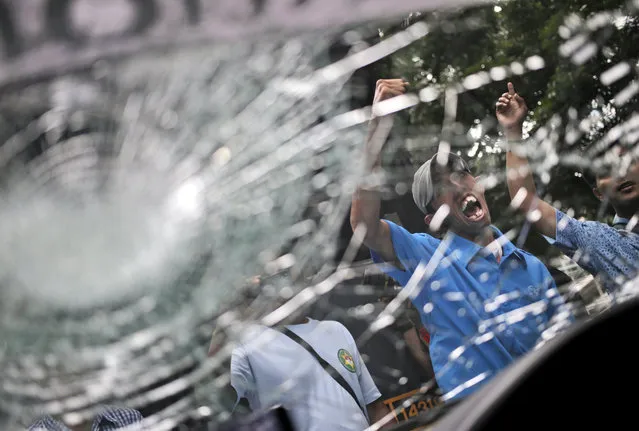 Taxi drivers are photographed through the smashed windshield of a taxi as they shouts slogans during a protest against competition from ride-hailing apps such as Uber and Grab in Jakarta, Indonesia, Tuesday, March 22, 2016. The windshield was allegedly smashed by drivers of a rival motorcycle taxi hailing app. (Photo by Dita Alangkara/AP Photo)