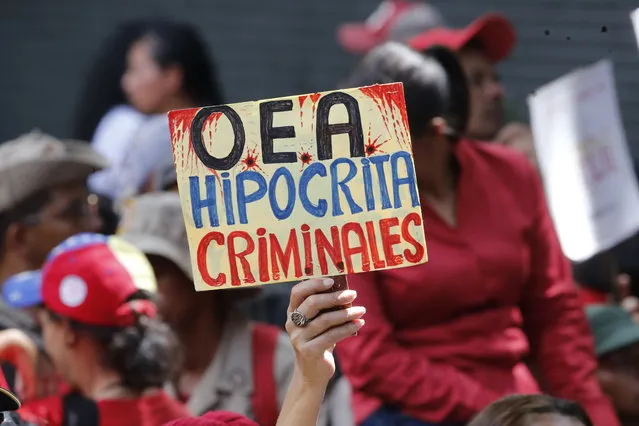 A supporter of Venezuela's president Nicolas Maduro, holds a sign that reads in Spanish “OAS Hypocrites, Criminals” during a government rally in Caracas, Venezuela, Saturday, April 27, 2019. The Trump administration has added Venezuelan Foreign Minister Jorge Arreaza to a Treasury Department sanctions target list as it increases pressure on embattled President Nicolas Maduro. (Photo by Ariana Cubillos/AP Photo)