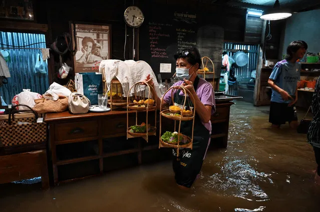 This photo taken on October 7, 2021, shows an employee serving desserts at the Chaopraya Antique Cafe, as flood water from the Chao Phraya River surges into the restaurant, in Nonthaburi province north of Bangkok. (Photo by Lillian Suwanrumpha/AFP Photo)