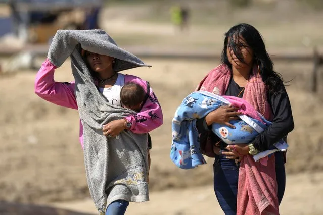 Women carry babies after arriving by boat from La Bulla Loca mine, which collapsed, in La Paragua, Bolivar state, Venezuela, Friday, February 23, 2024. The collapse of the illegally operated open-pit gold mine in a remote area of central Venezuela killed at least 16 people. (Photo by Ariana Cubillos/AP Photo)