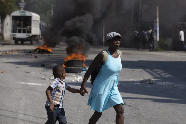 A child, walking hand-in-hand with his mother, looks over at a burning barricade set up by friends and relatives of James Philistin who was kidnapped last night, in Port-au-Prince, Haiti, Wednesday, November 24, 2021. (Photo by Joseph Odelyn/AP Photo)