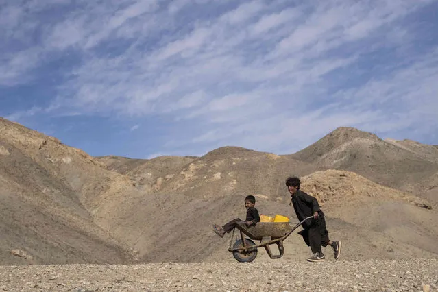 A boy pushes a wheelbarrow with canisters and his younger brother, on their way to collect water from a stagnant pool, about 3 kilometers (2 miles) from their home in Kamar Kalagh village outside Herat, Afghanistan, Friday, November 26, 2021. Afghanistan’s drought, its worst in decades, is now entering its second year, exacerbated by climate change. (Photo by Petros Giannakouris/AP Photo)