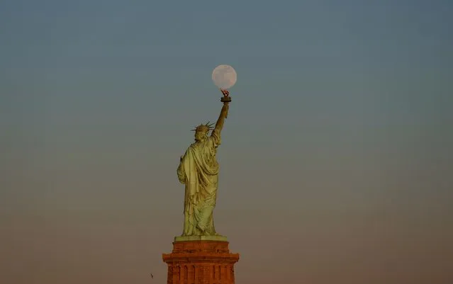 The Pink Moon, illuminated at 99 percent, rises behind the Statue of Liberty as the sun sets in New York City on April 22, 2024, as seen from Jersey City, New Jersey. (Photo by Gary Hershorn/Getty Images)