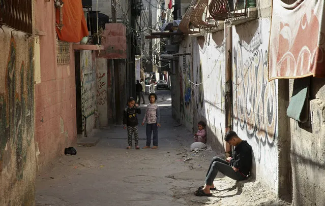 In this April 21, 2019 photo, a Palestinian teenager sits in an alley as children play in front of their family house, in the Shati refugee camp, in Gaza City. The blockade Israel and Egypt imposed on Gaza after the Hamas militant group took power in 2007 has ravaged the economy. The skyrocketing unemployment rates, combined with foreign aid cuts and Hamas' mismanagement, has left thousands of families dependent on food aid and social welfare. Many young Gazans have been forced to put off their dreams of marriage because they cannot afford it. (Photo by Adel Hana/AP Photo)