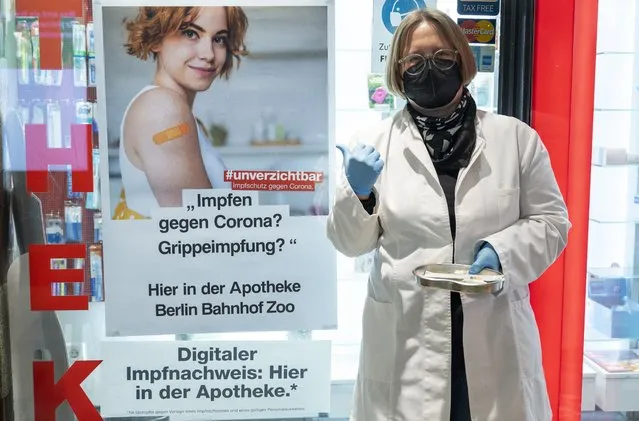 Sandra Fundel, pharmacist at the pharmacy at Bahnhof Zoo, stands outside the pharmacy with vaccination paraphernalia, next to a poster advertising the Corona vaccination in Berlin, Germany, Monday, February 7, 2022. Pharmacists in the country are scheduled to begin offering vaccinations Tuesday, after parliament changed the rules so that they, dentists and vets could administer the shoots. (Photo by Christophe Gateau/dpa via AP Photo)