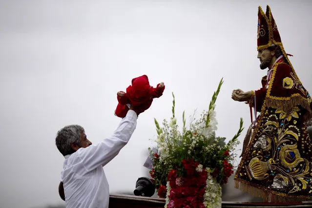 A fisherman holds a baby in front of the statue of Saint Peter asking for good health for the child, during a procession in Lima, Peru, Monday, June 29, 2015. (Photo by Rodrigo Abd/AP Photo)