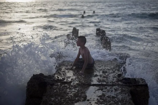 A Muslim boy sits on an old wave breaker at the Mediterranean Sea during the last day of the Eid al-Fitr holiday as the sun sets in Tel Aviv, Israel, Sunday, July 19, 2015. (Photo by Ariel Schalit/AP Photo)