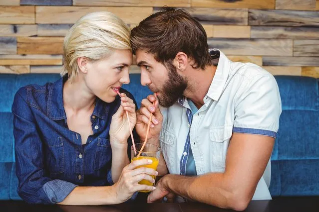 Cute couple on a date sharing a glass of orange juice. (Photo by Wavebreak Media ltd/Alamy Stock Photo)