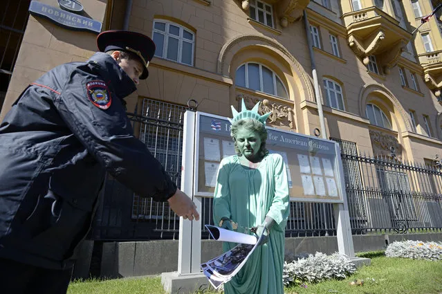 A woman gives pictures of riots in the USA to a Russian policeman as she wears a Statue of Liberty suit during a protest in front of the US embassy in central Moscow on September 16, 2014. (Photo by Alexander Nemenov/AFP Photo)