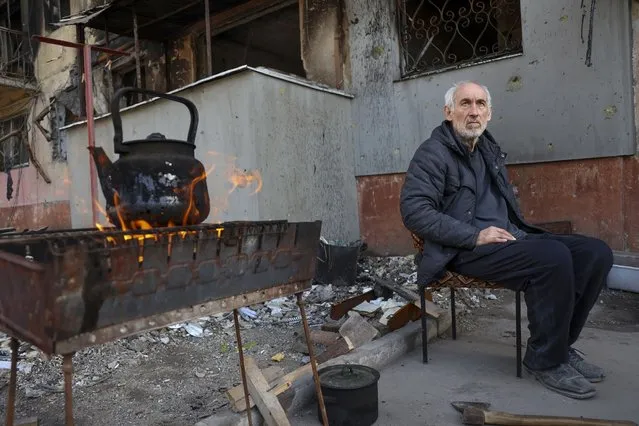 A local man sits in front of an apartment building damaged from heavy fighting as he waits for the kettle to boil in an area controlled by Russian-backed separatist forces in Mariupol, Ukraine, Tuesday, April 26, 2022. (Photo by Alexei Alexandrov/AP Photo)