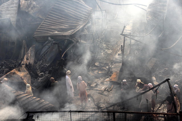 People watch as Afghans firefighters work to extinguish a fire that engulfed a vehicle spare parts market in Spin Boldak District in Kandahar, Afghanistan, 19 July 2024. According to the district governor Mullah Abdullah Bashir, the fire that broke out in Boldak District in Kandahar main vehicle spare parts market destroyed more than 2,500 shops and millions of dollars were damaged in this fire. (Photo by Qudratullah Razwan/EPA)