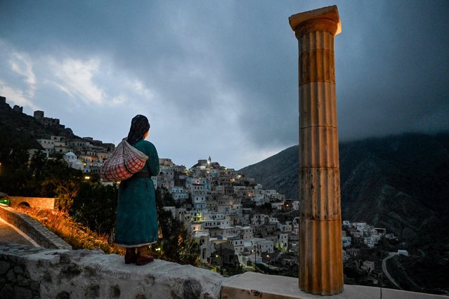 A woman stands in front of a sculpture dedicated to the women of Olympos at the remote village of Olympos on the island of Karpathos on May 5, 2023. In the north of the Greek island of Karpathos, the hillside village of Olympos is home to one of the few matriarchal societies in Greece that resists tourism and lifestyle standardisation. (Photo by Louisa Gouliamaki/AFP Photo)