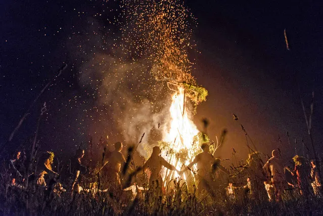 Young people wearing Belarus traditional clothes and wreaths dance around a bonfire as they celebrate the Ivan Kupala night, an ancient heathen holiday, held in the countryside near Minsk, on June 19, 2016. People celebrate Kupala Night with bonfires that last throughout the night with some leaping over the flames as it is believed that the act of jumping over the bonfire cleanses people of illness and bad luck. (Photo by Maxim Malinovsky/AFP Photo)